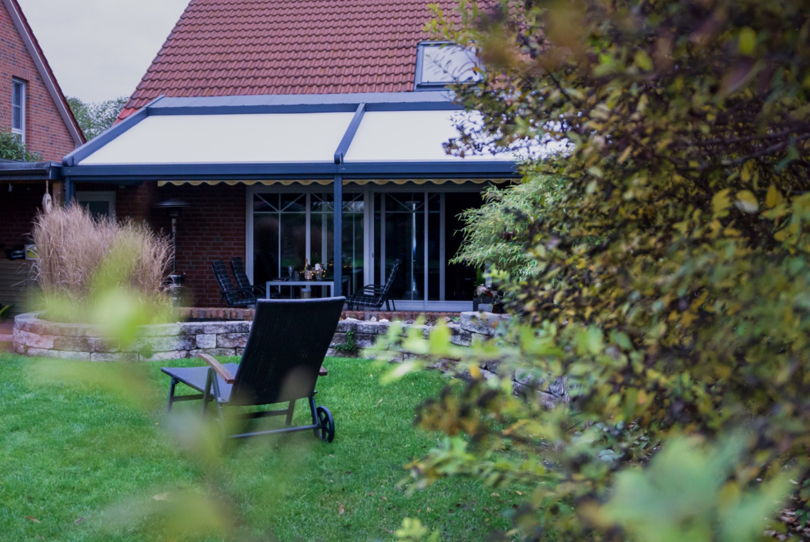 A modern pergola system by Palmiye Global, enhancing the outdoor space of a house with a shaded seating area and stylish design, surrounded by lush greenery.