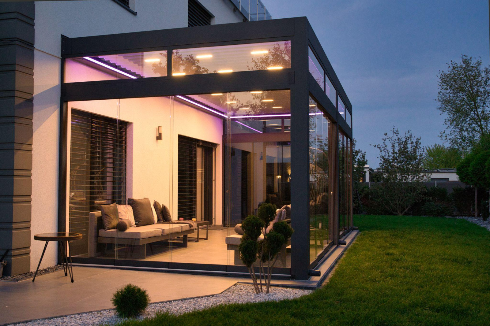 A sleek modern residence with a glass-walled patio, highlighting elegant outdoor seating areas complemented by a pergola.