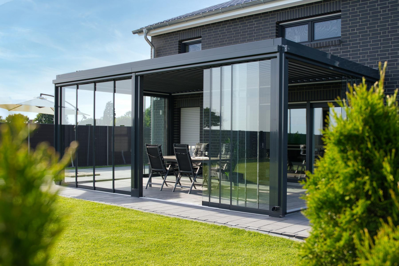 A glass patio featuring a table and chairs, ideal for outdoor seating under a stylish pergola system.