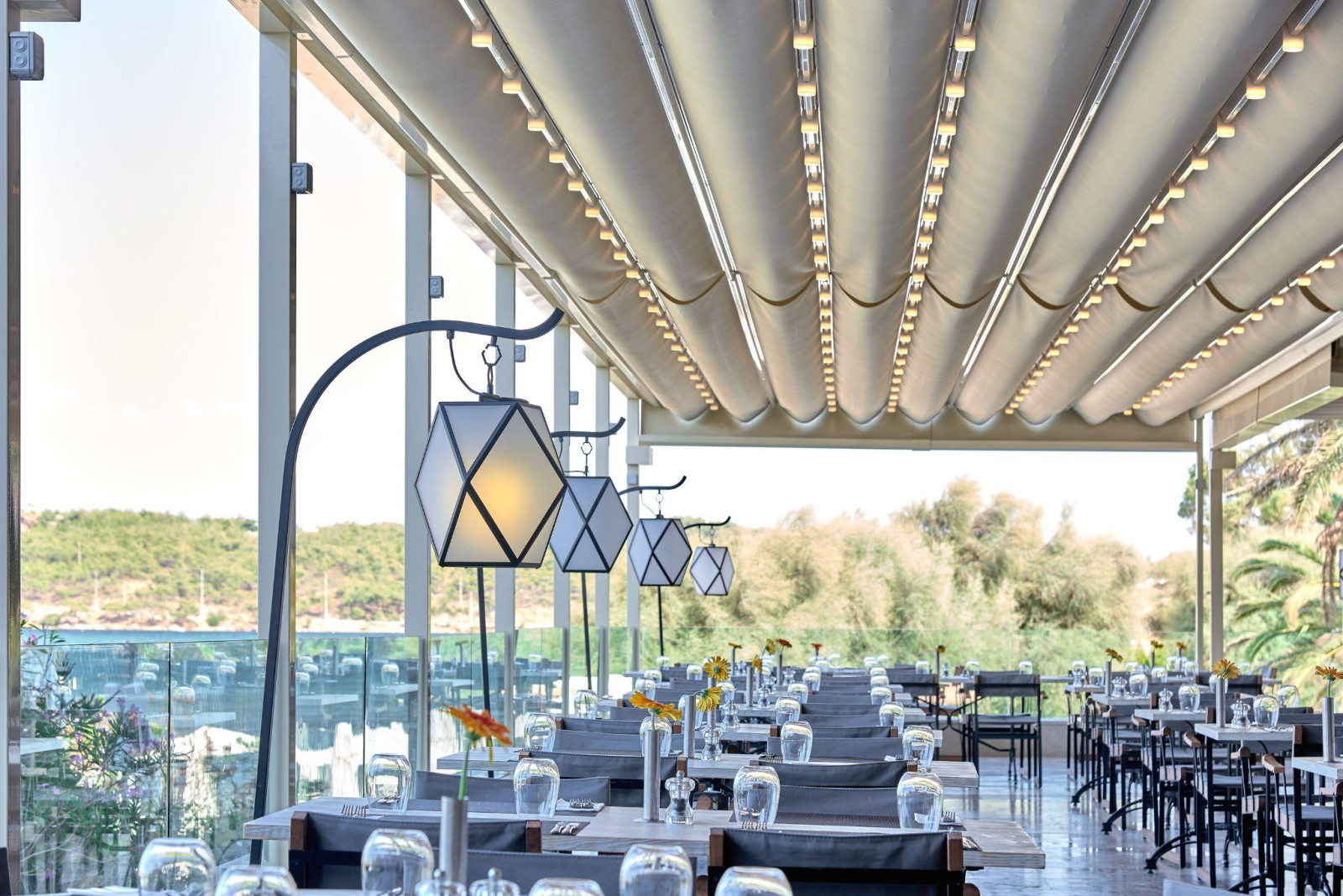 Outdoor dining area on a restaurant rooftop, equipped with tables and chairs beneath a modern pergola structure.