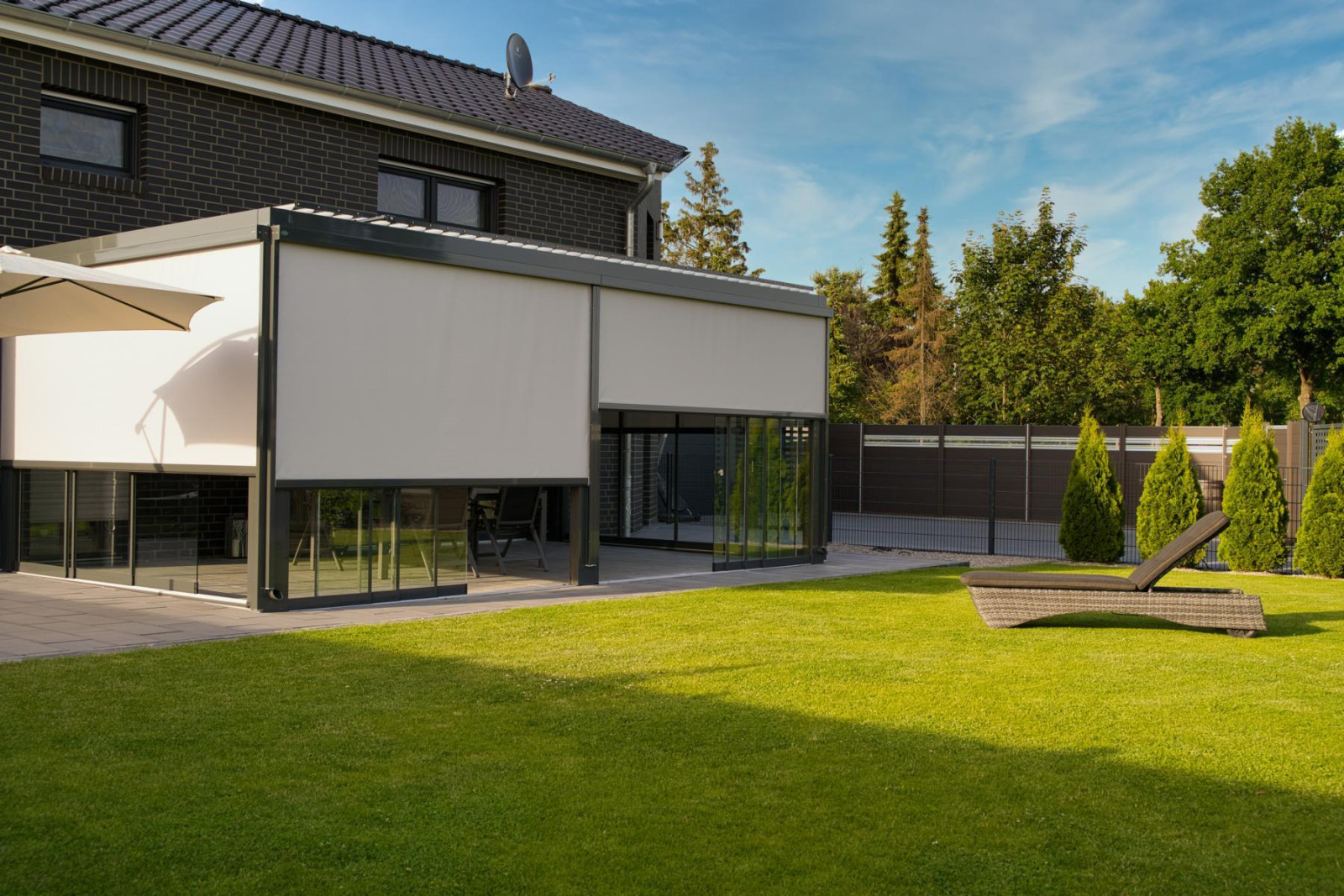 A large house featuring an expansive patio adorned with a pergola system and blinds for shade and comfort.