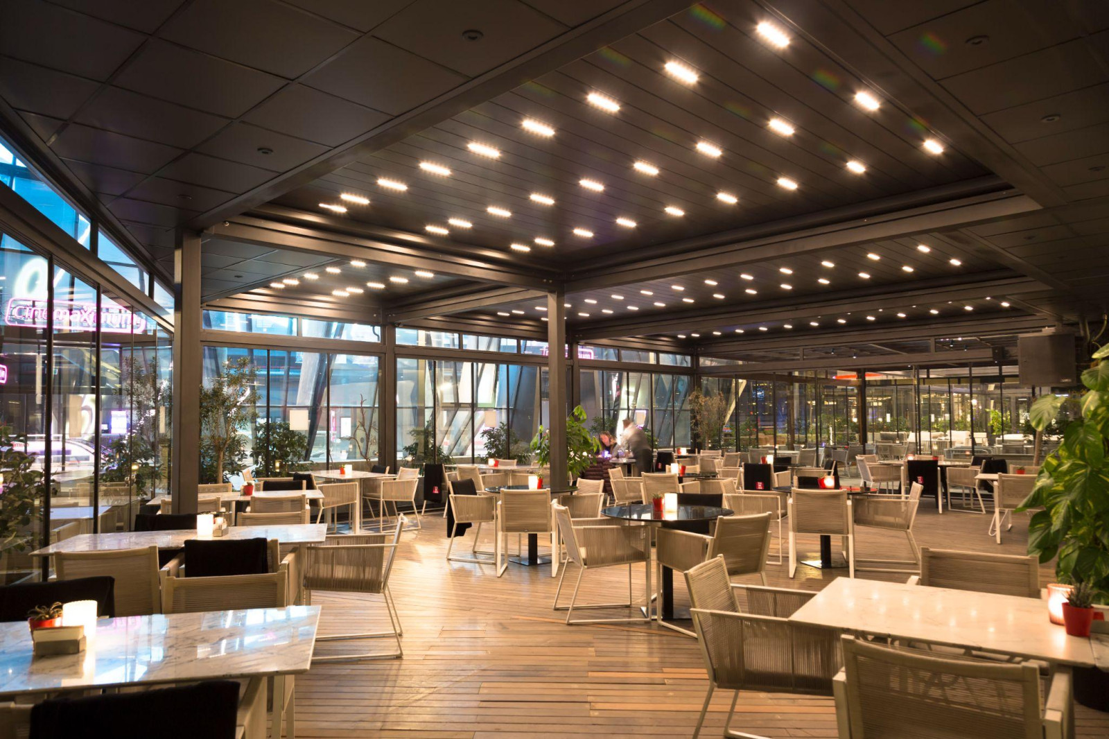 A restaurant featuring tables and chairs outside a glass wall, showcasing pergola solutions for outdoor dining.