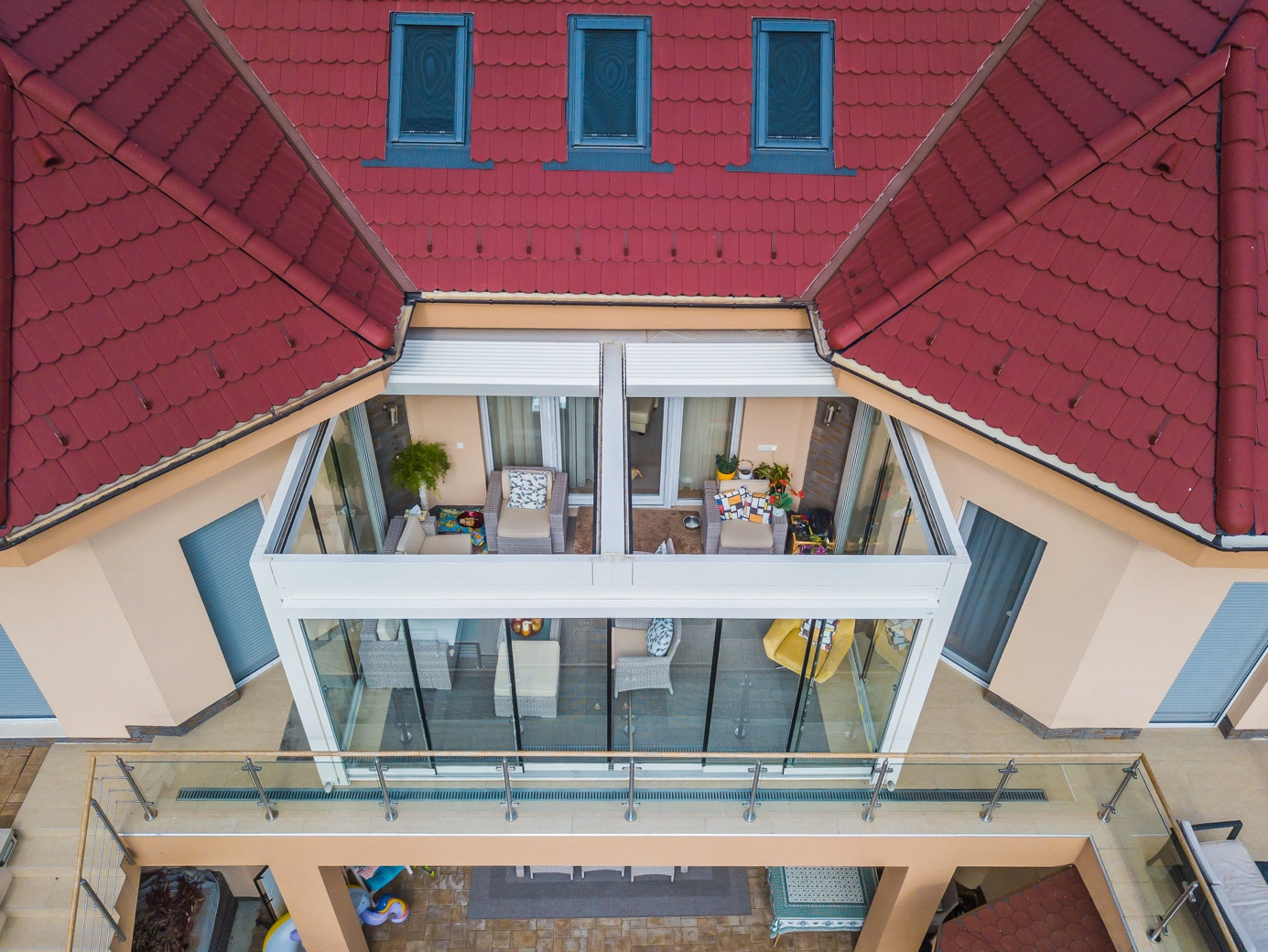 Kırmızı çatılı ve cam duvarlara sahip bir ev, Palmiye Global tarafından tasarlanmış rüzgara dayanıklı pergola sistemiyle tamamlanıyor.