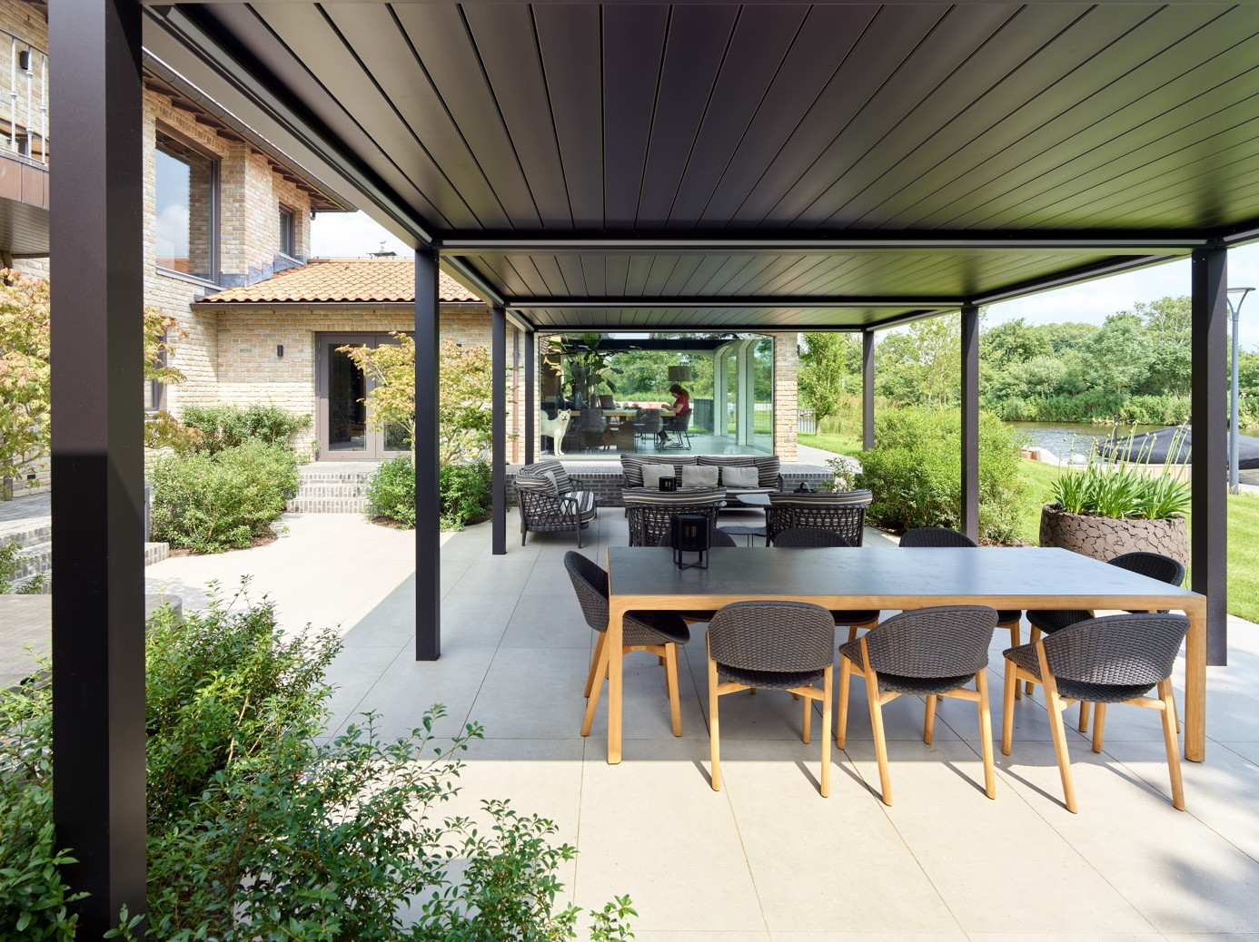 Large aluminum pergola system with retractable roof for shaded garden dining and lounge areas