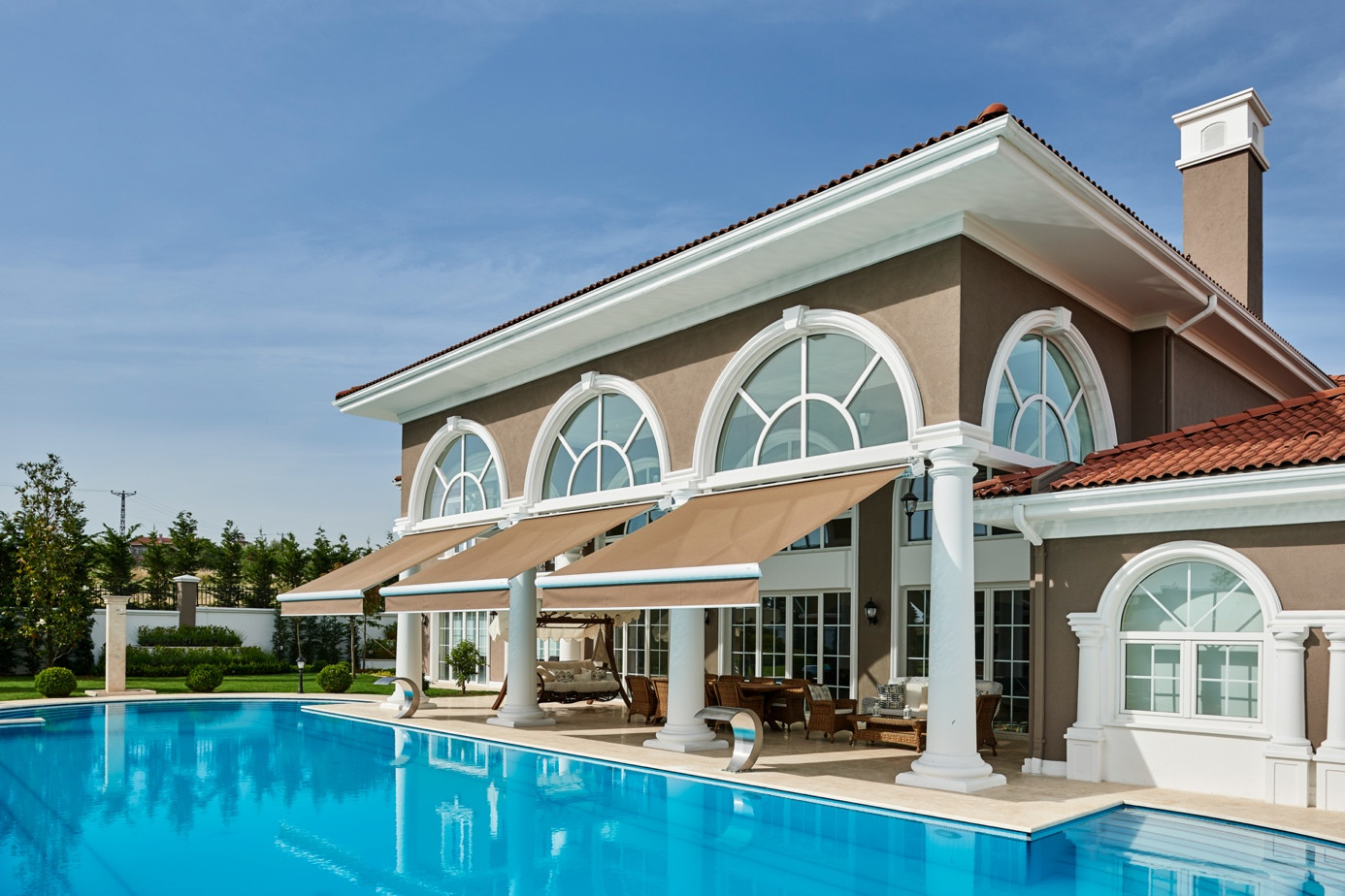 Beige retractable awning systems matching the façade color of a luxury villa with poolside outdoor living space