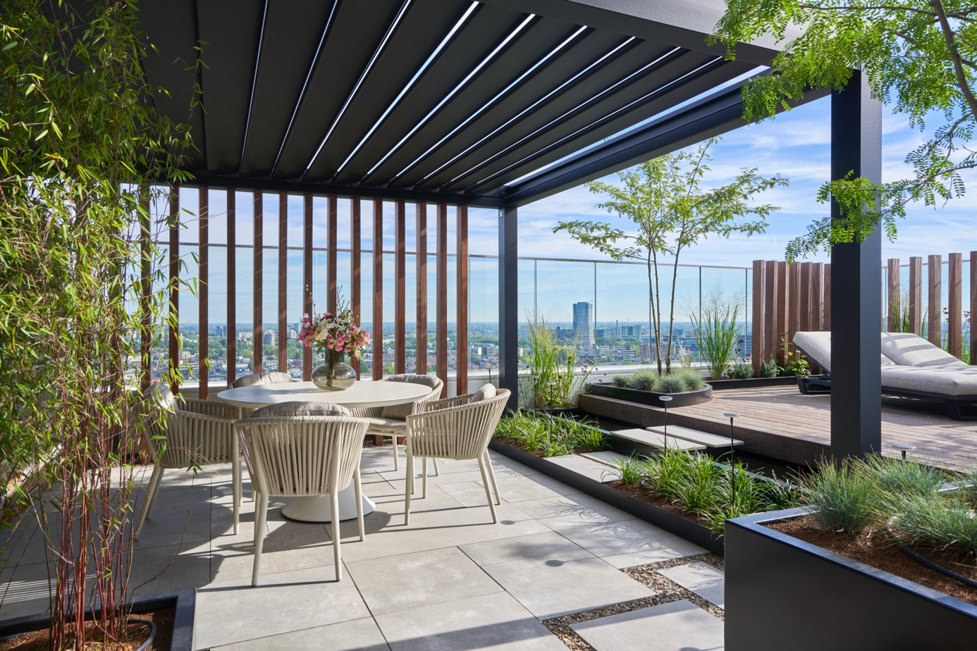 Şehir manzaralı terasta gölgelendirme sağlayan siyah bioklimatik pergola sistemi