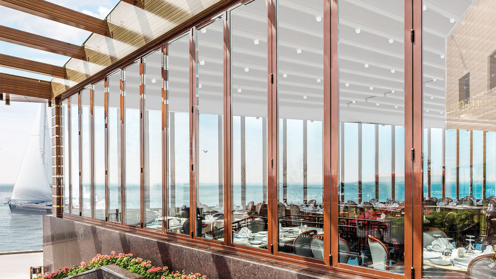 Deniz manzaralı restoran cephesinde, kahverengi çerçeveli katlanır cam panellerin kapalı görünümü.